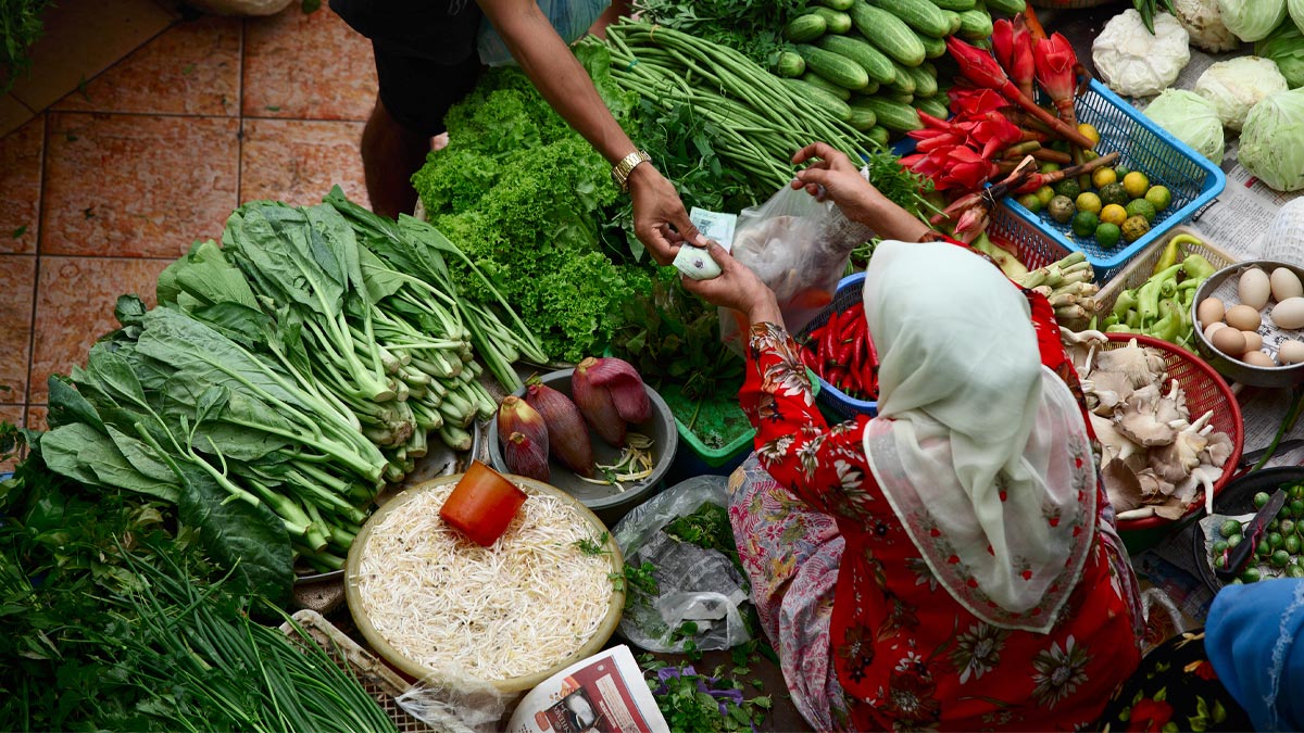 A man pays for vegetables in an outdoor grocery market.