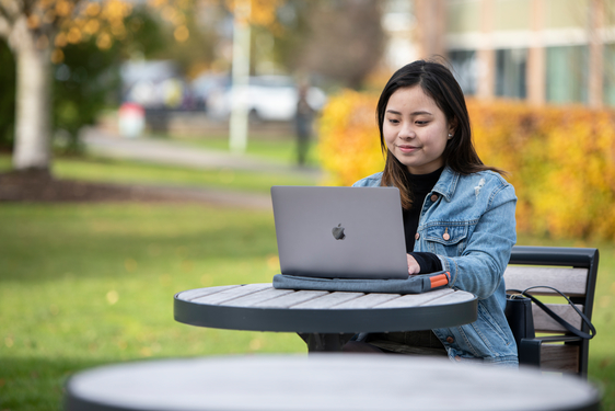 a student sits at a table outdoors with their laptop