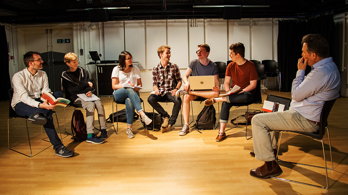 A group of students and lecturers sat around in a studio in a group discussion