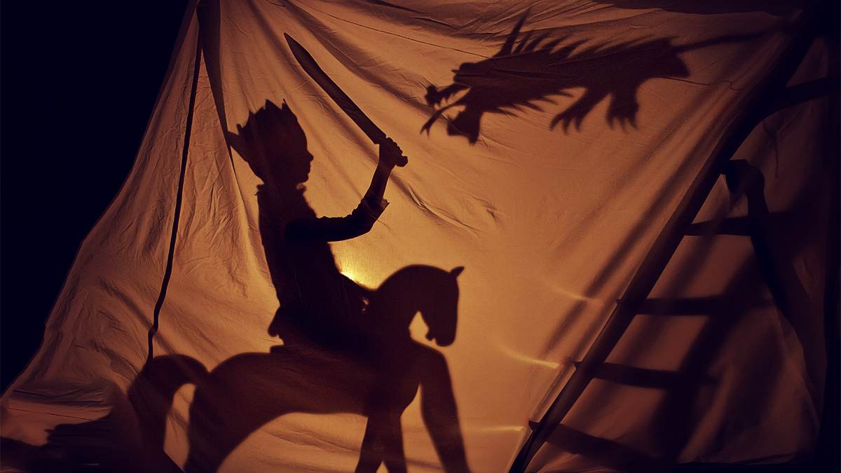Shadowplay images against a white sheet of a knight on a horse battling a dragon