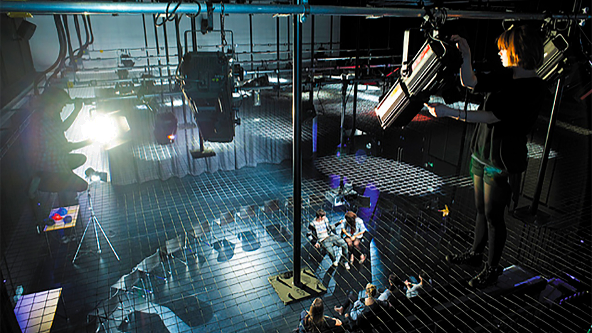 View of a performance space from above on the grid rigging, with a student adjusting a spotlight