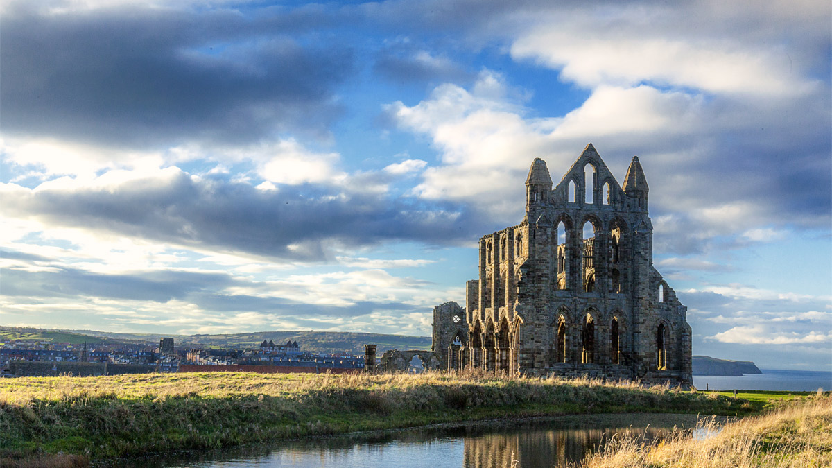 landscape shot of abbey ruins on a green field against a cloudy blue sky