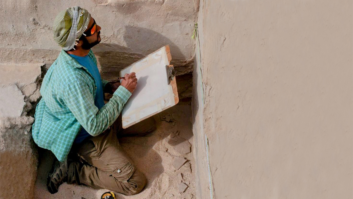 Rizwan Ahmad kneeling inside an excavation site and taking notes
