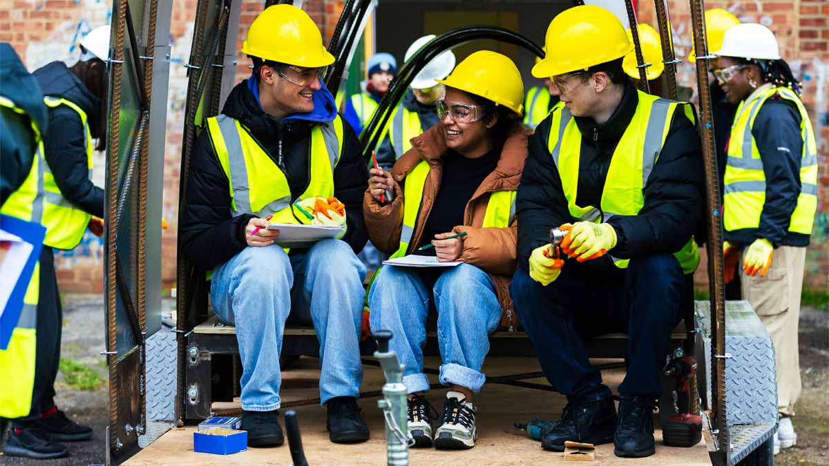 Students smiling during an architecture visit, wearing high-vis PPE safety clothing.