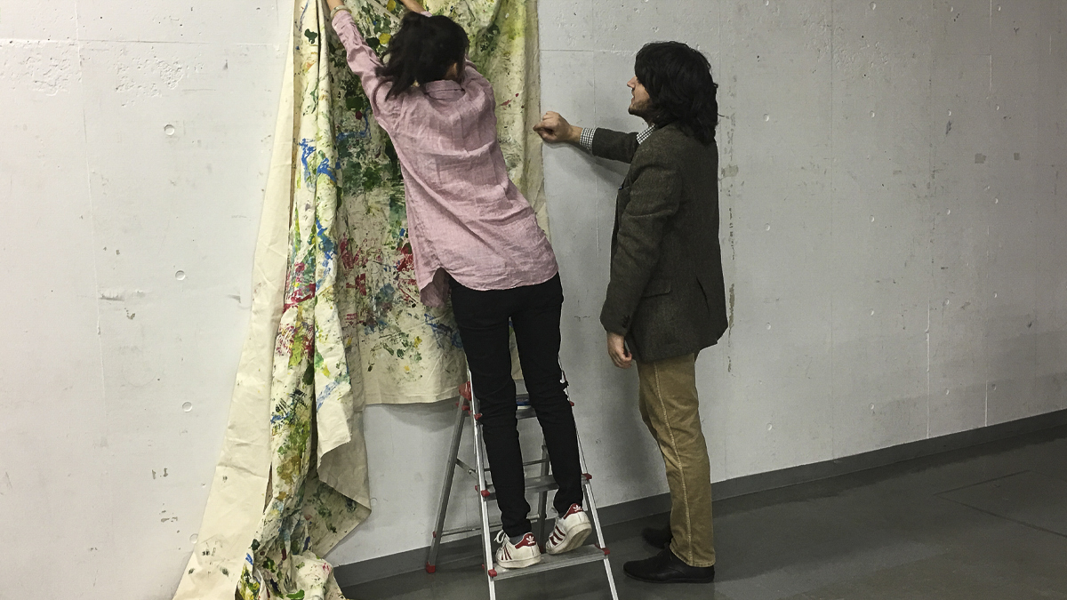 Two students hanging a piece of artwork on the wall