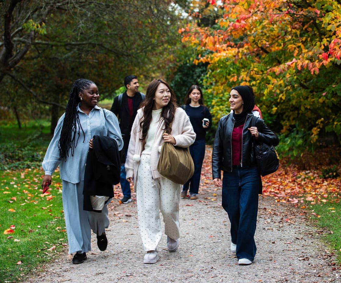 Students walking together through a leafy campus pathway in autumn.