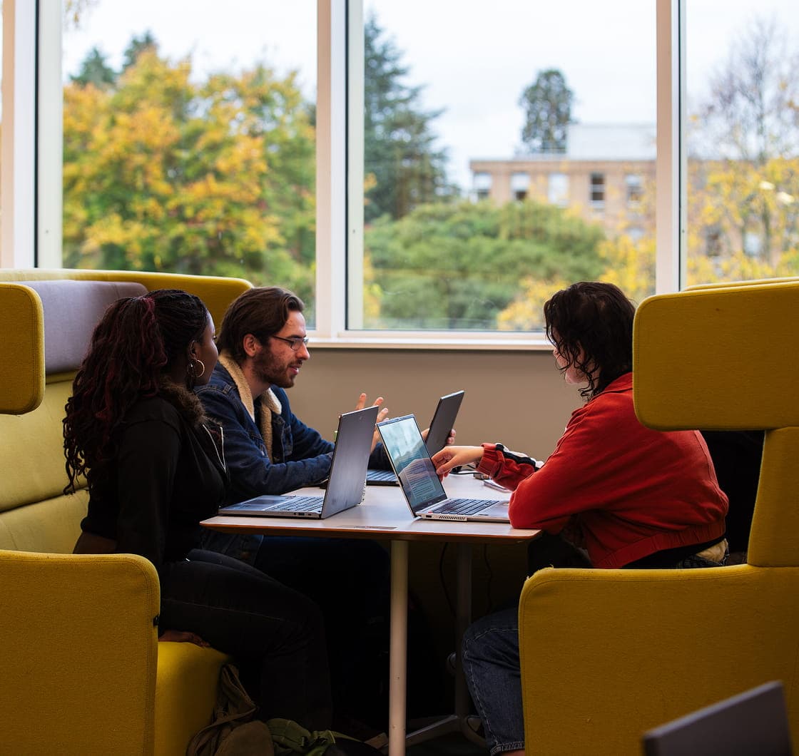 Students working together on laptops in a collaborative study space on campus.