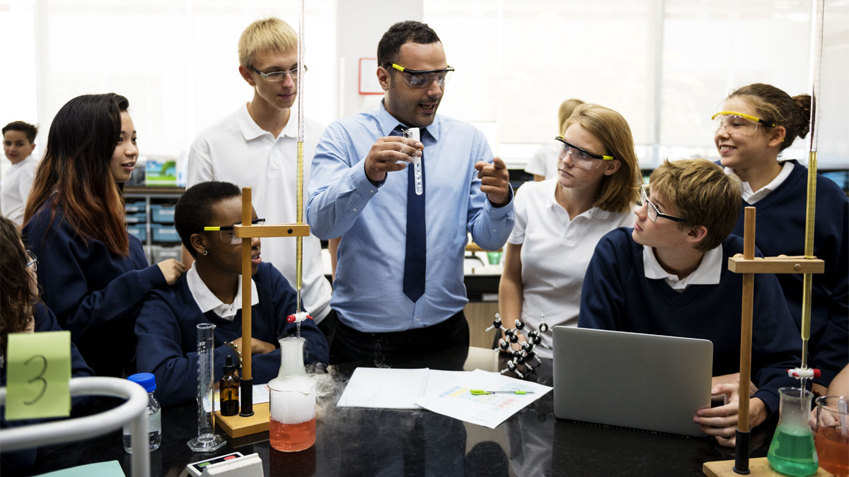 Students gathered round a science teacher who is explaining an experiment