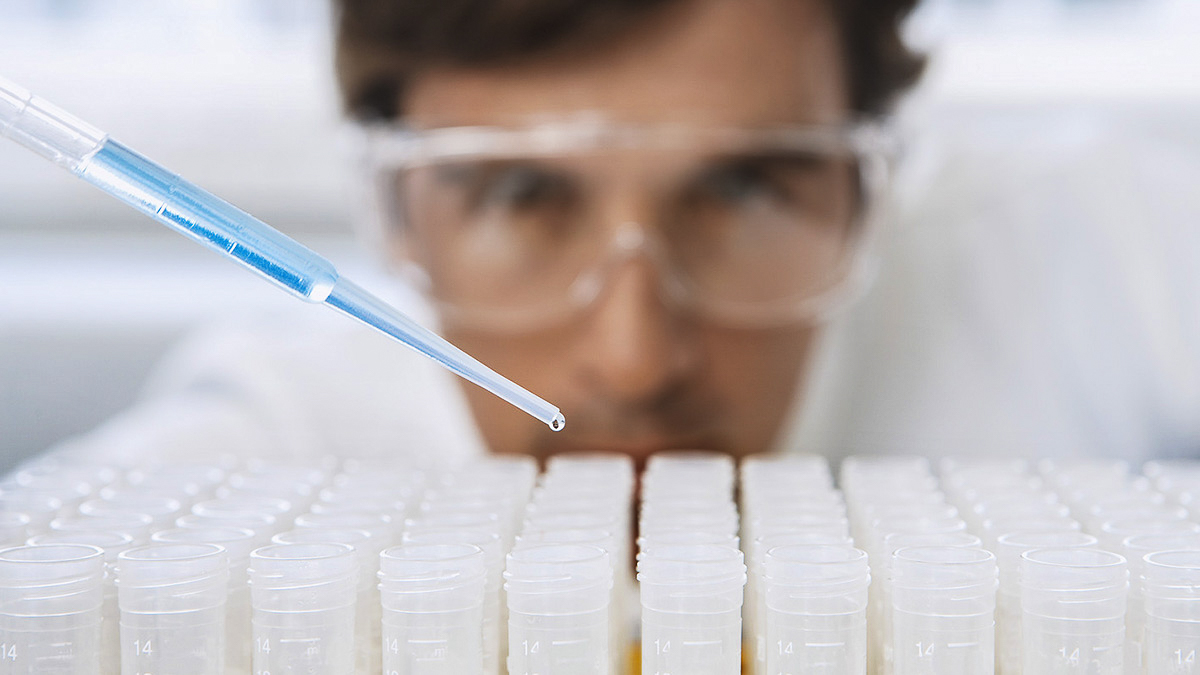 Scientist dropping chemical from pipette into test tubes