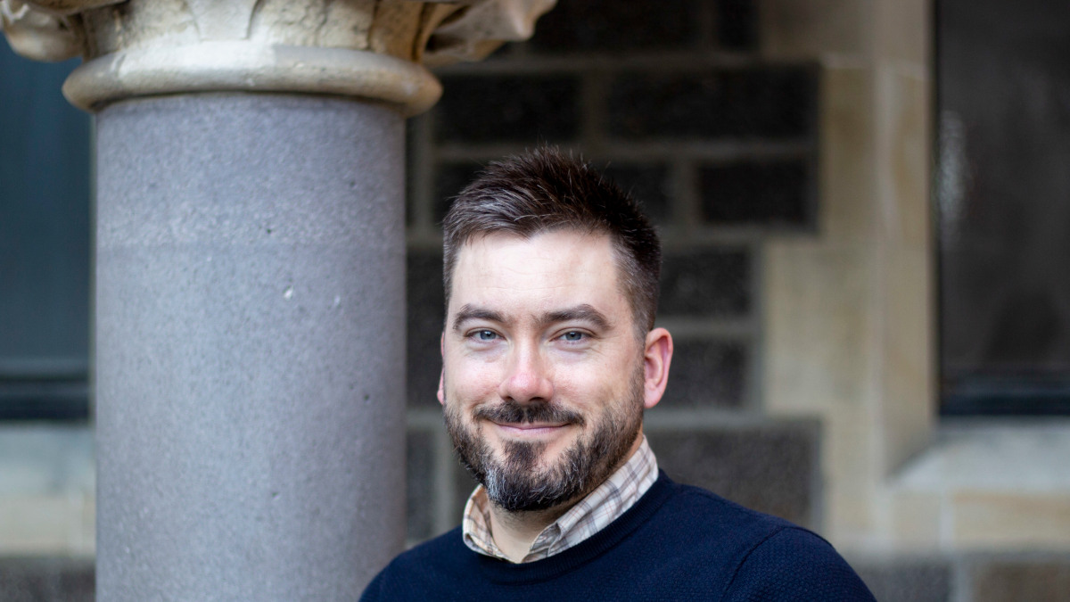 Dylan James standing beside a stone column with a brick and stone wall in the background
