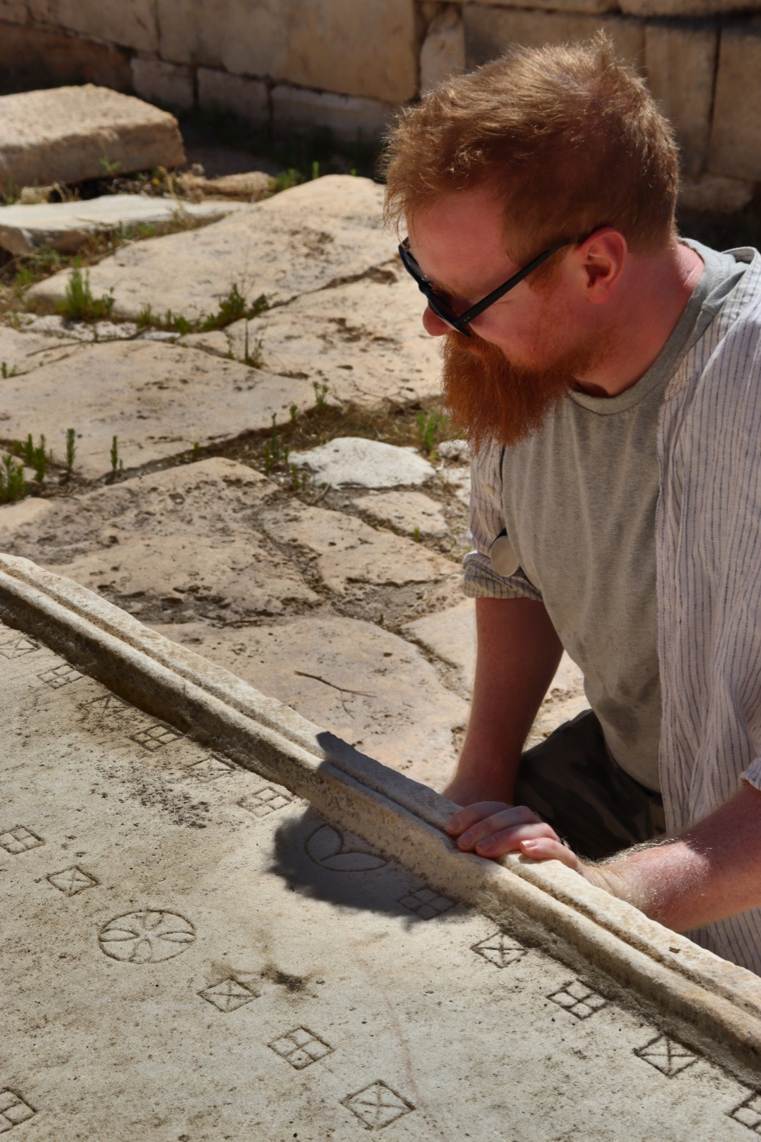 A researcher examining an ancient carved stone surface featuring geometric patterns and game board markings at an archaeological site.