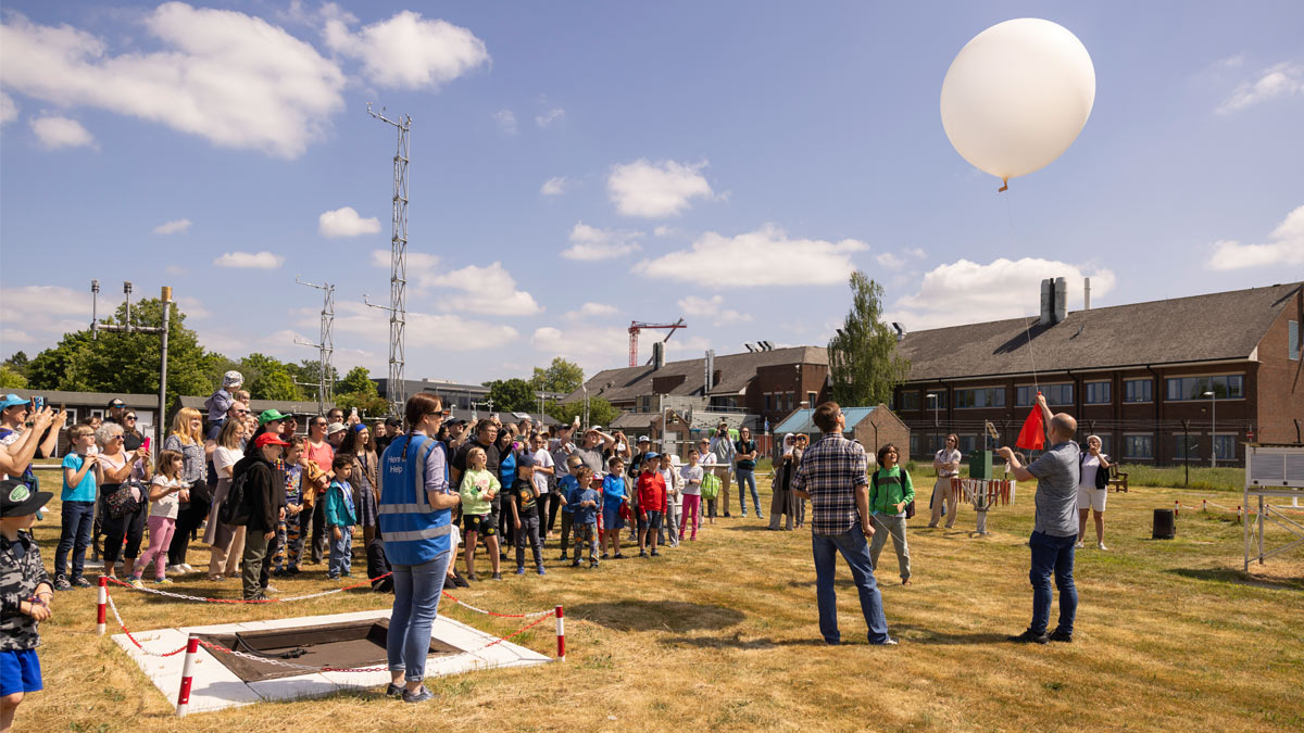 University of Reading's Community Festival 2025, a large group of people are gathered outside the Atmospheric Observatory in the sun, watching the launch of a weather balloon.