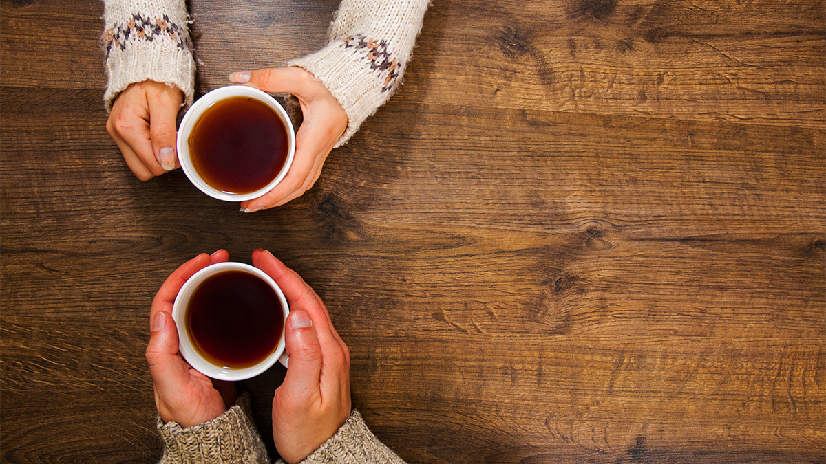 Aerial shot of two people sat at a wooden table with cups of tea