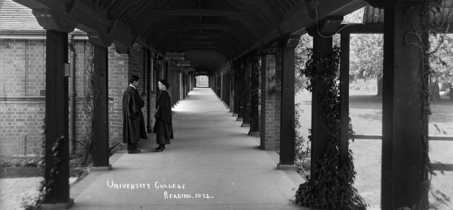 Black and white photograph of the cloisters at London Road campus. Two students in robes stand in the mid-ground