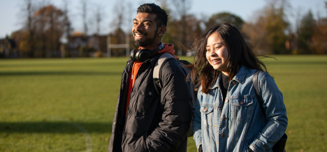 Two students walking on a field laughing with eachother.