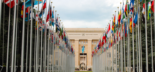 Two rows of international flags leading to a United Nations building. 