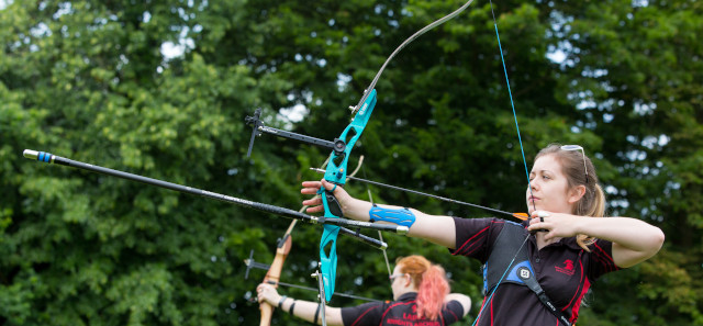 There are two students getting ready to release their arrow from their crossbow. One girl is in the background, and one is in the foreground. 