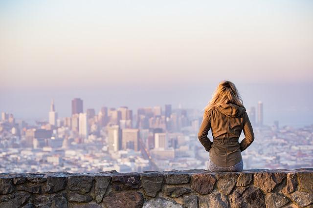 Woman sits on a wall looking out over a distant cityscape