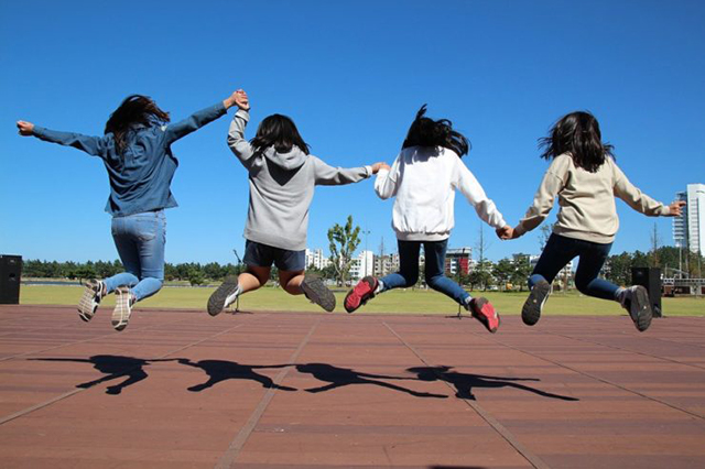 Four girls jump in the air in an outdoor green space