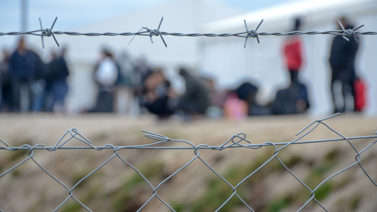 visitors to a refugee camp seen through a barbed wire fence