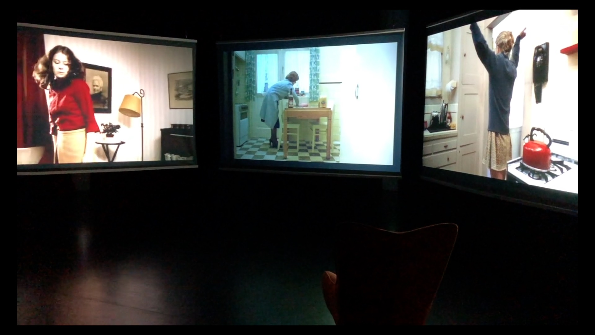 Three big screens showing movie scenes in front of a chair.