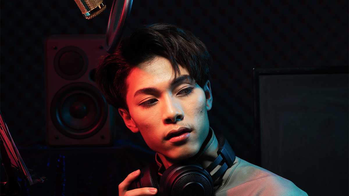 Male student with headphones round his neck, standing in a recording studio