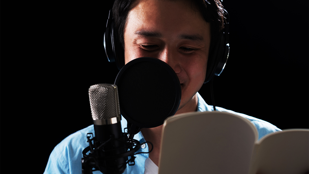 Close up of male student wearing headphones reading from a script and speaking into microphone