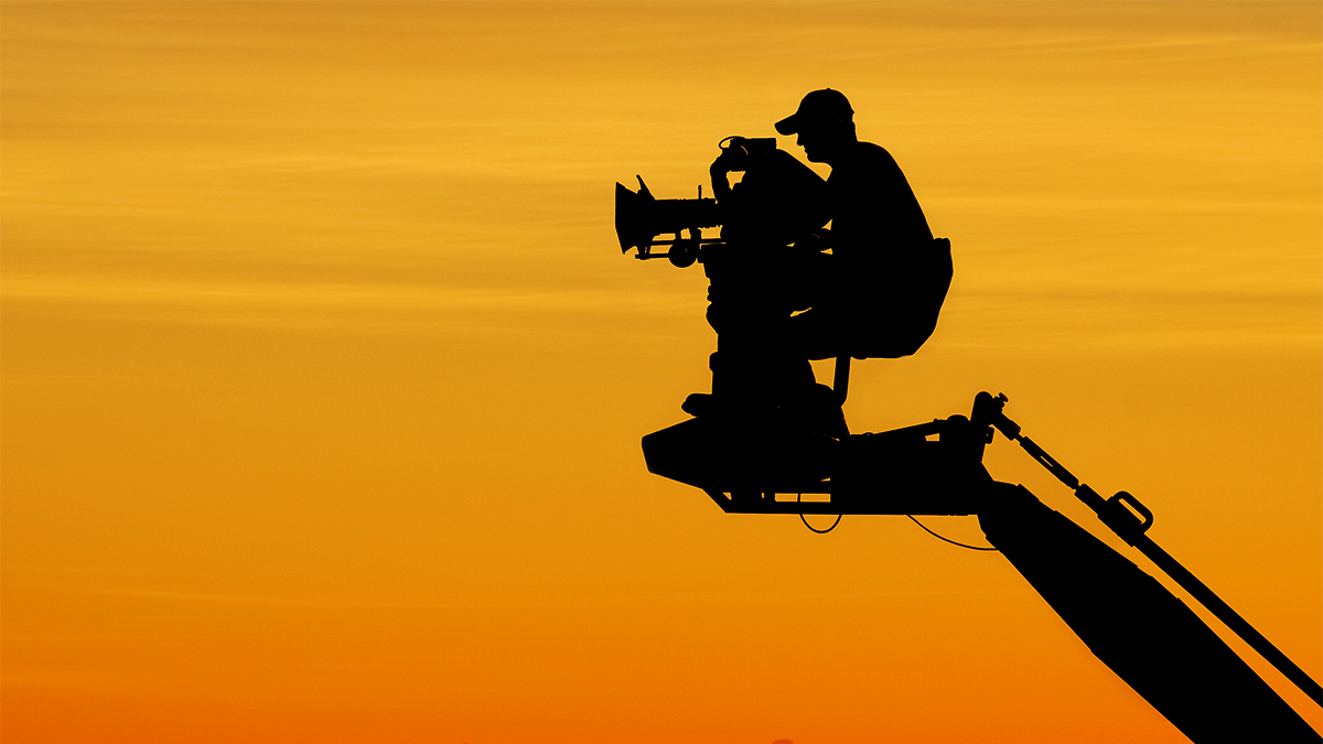 Silhouette of a film cameraman on a rig with an orange sky in the background