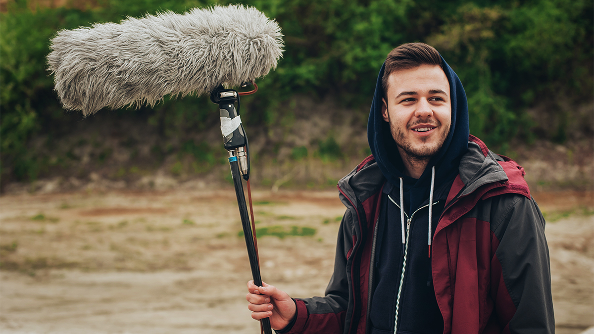 Film student holding a boom microphone as part of a shoot on location