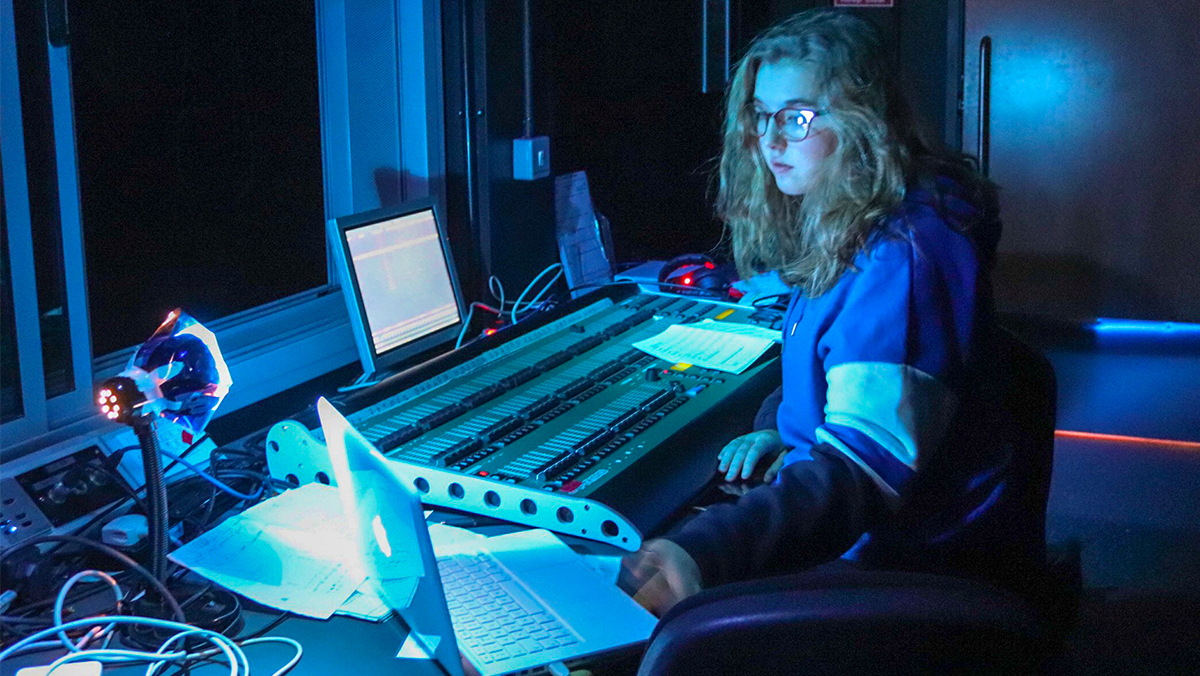 A film student in a dark sound studio sat at a mixing board
