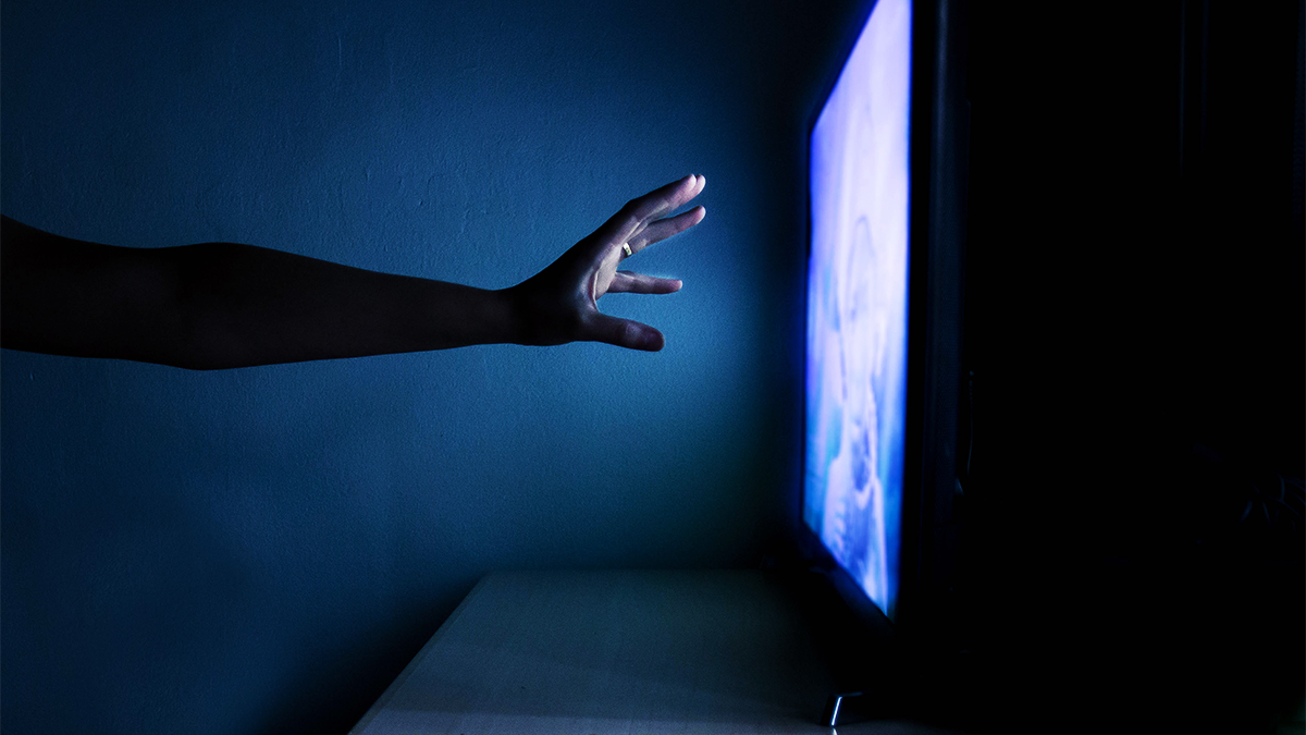 Hand reaching towards television that is switched on