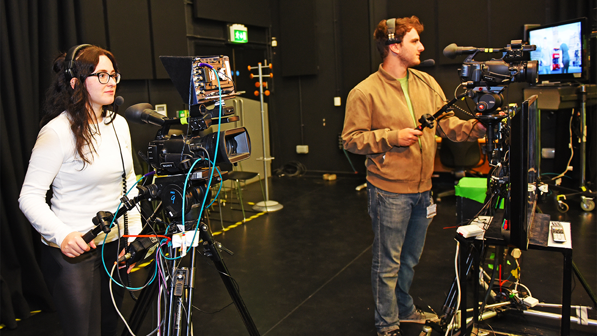 Two students each standing behind a film camera filming a project in the TV and film studio