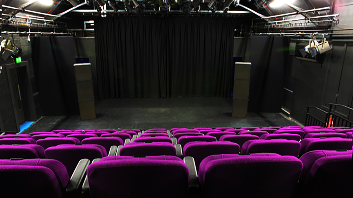 A versatile theatre space in Minghella Studios, the home of the Deparment of Film, Theatre and Television at the University of Reading. Purple seats face the stage, and there is full stage lighting equipment.