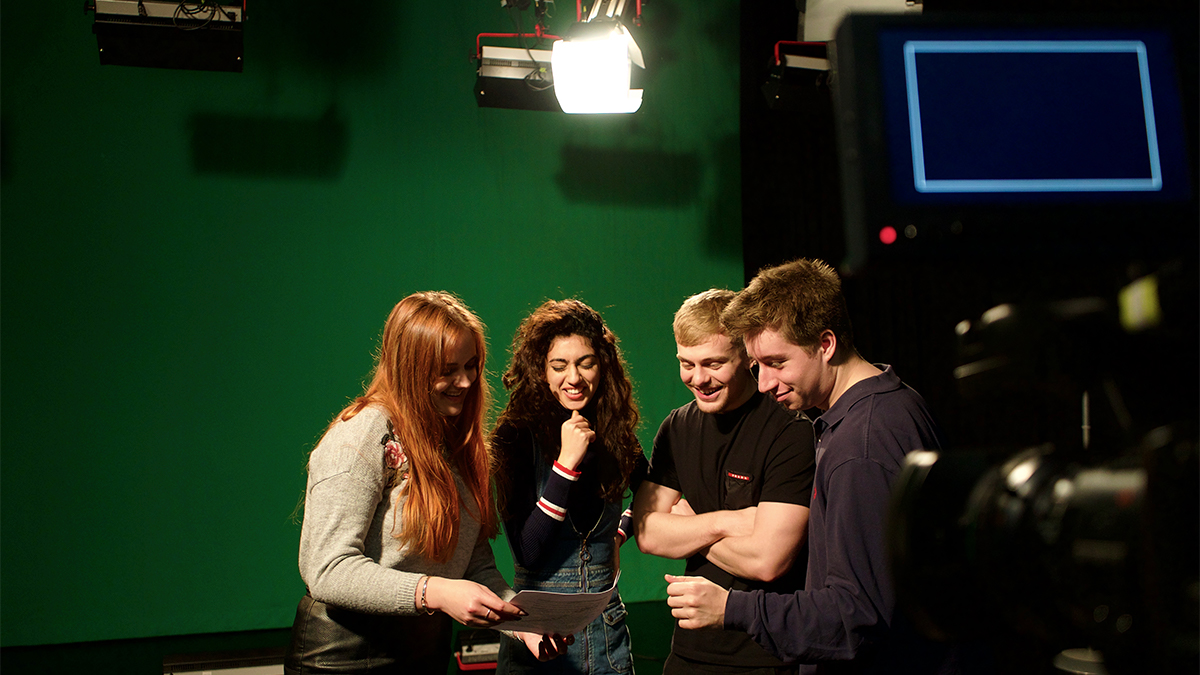 Four undergraduate students in a TV greenscreen studio looking over notes