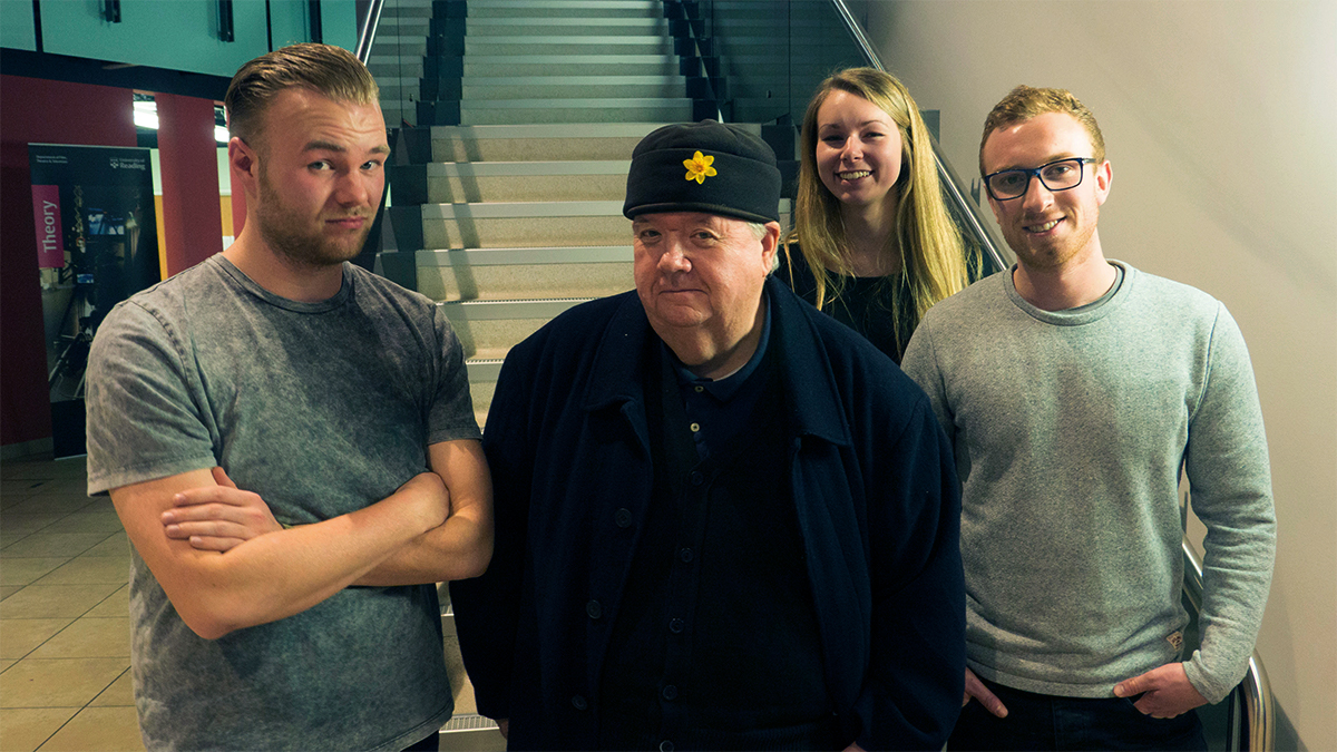 Visiting lecturer Ian McNeice with three students standing against a stairway in Minghella Studios