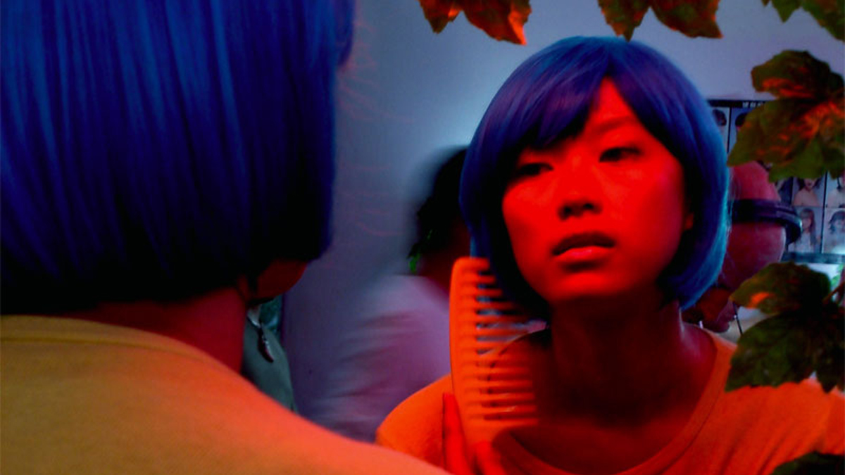 Chinese woman with blue hair looking at a mirror.