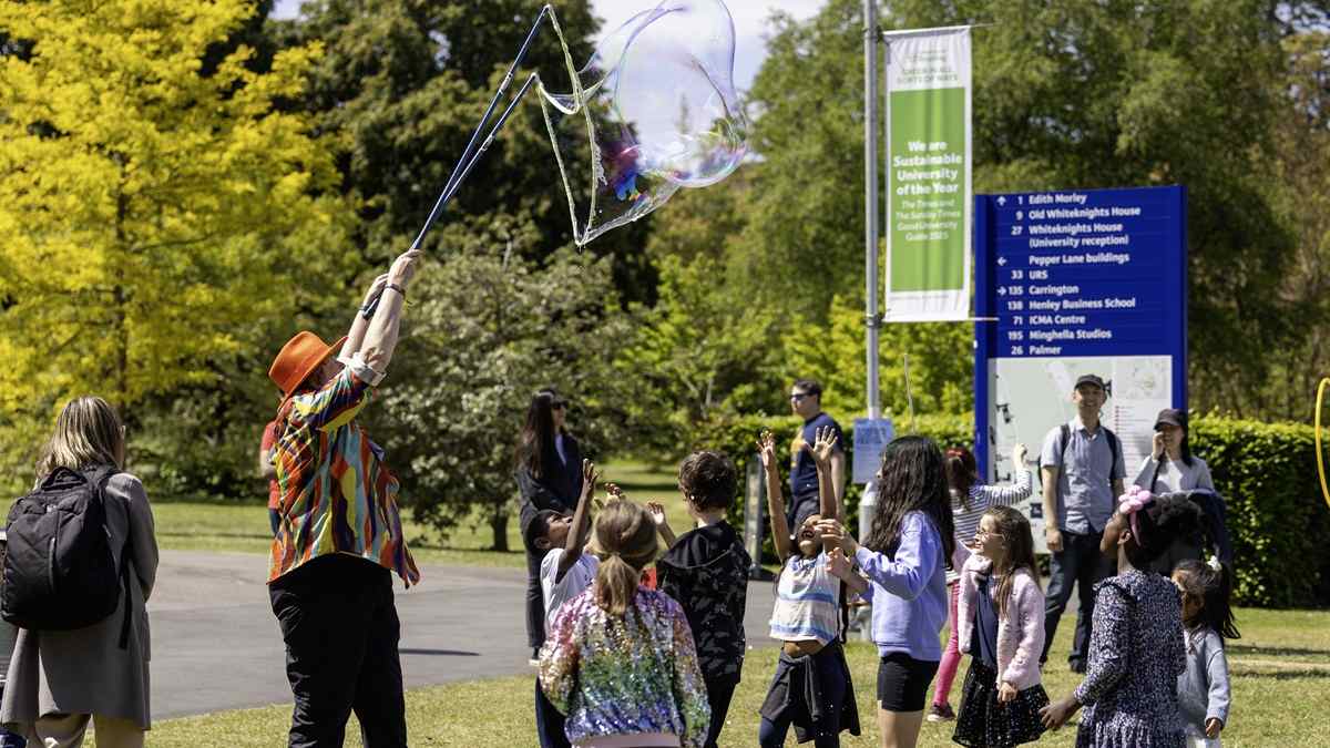 A brightly dressed entertainer blowing giant bubbles for children on Whiteknights campus