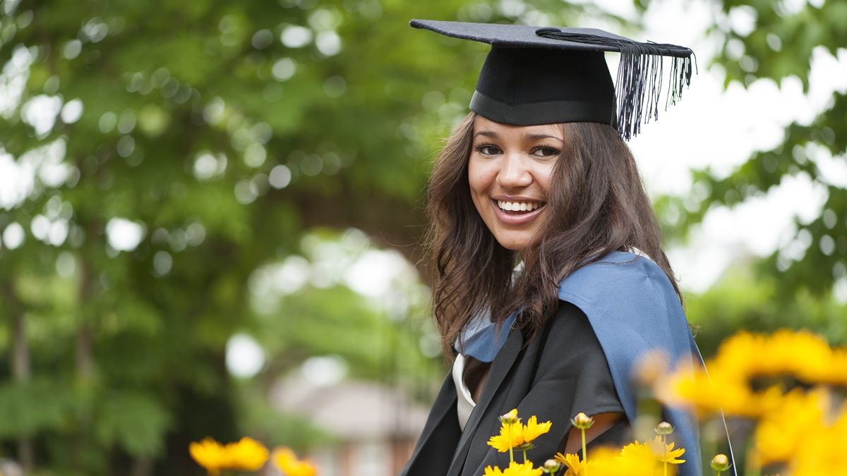 Female student in cap and gown with yellow flowers in the foreground