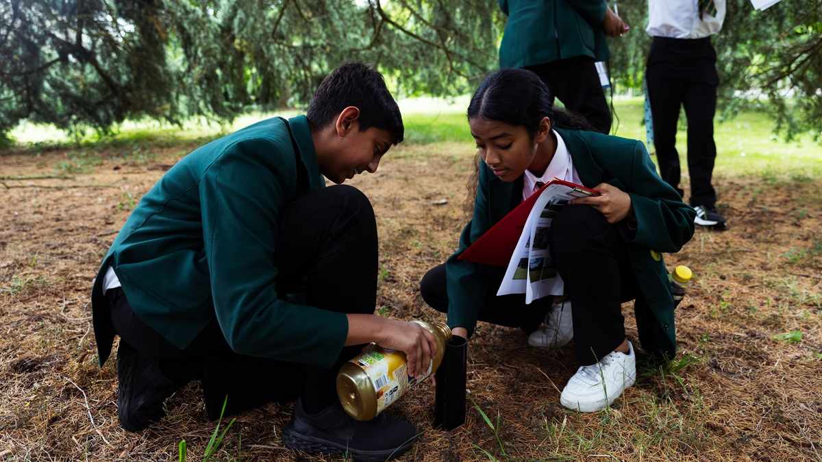 Two schoolchildren doing an experiment outside on the ground.