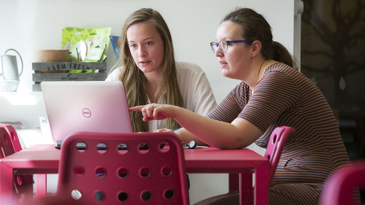 Two female students sitting at a table with their laptops