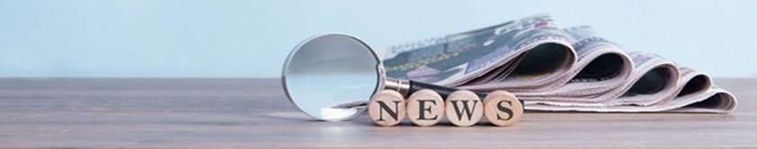 Stack of newspapers and a magnifying glass on a table with a sign that says 'News'
