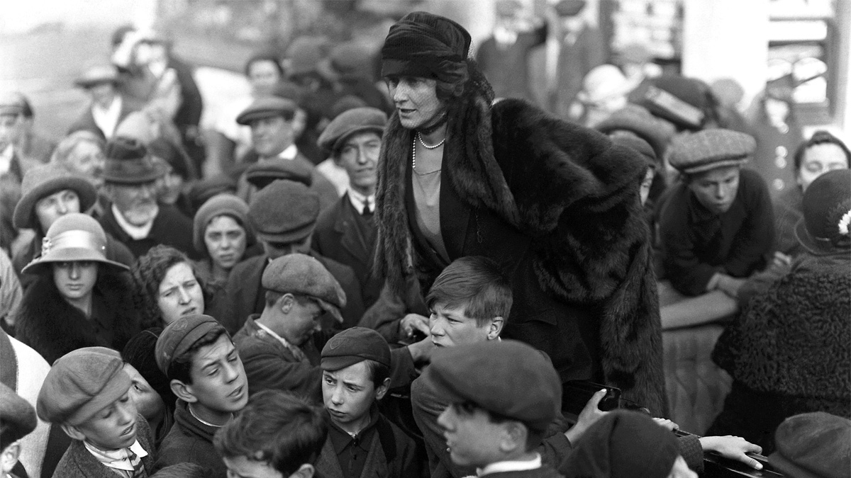 Nancy Astor sits on a mans shoulders in a crowd of people