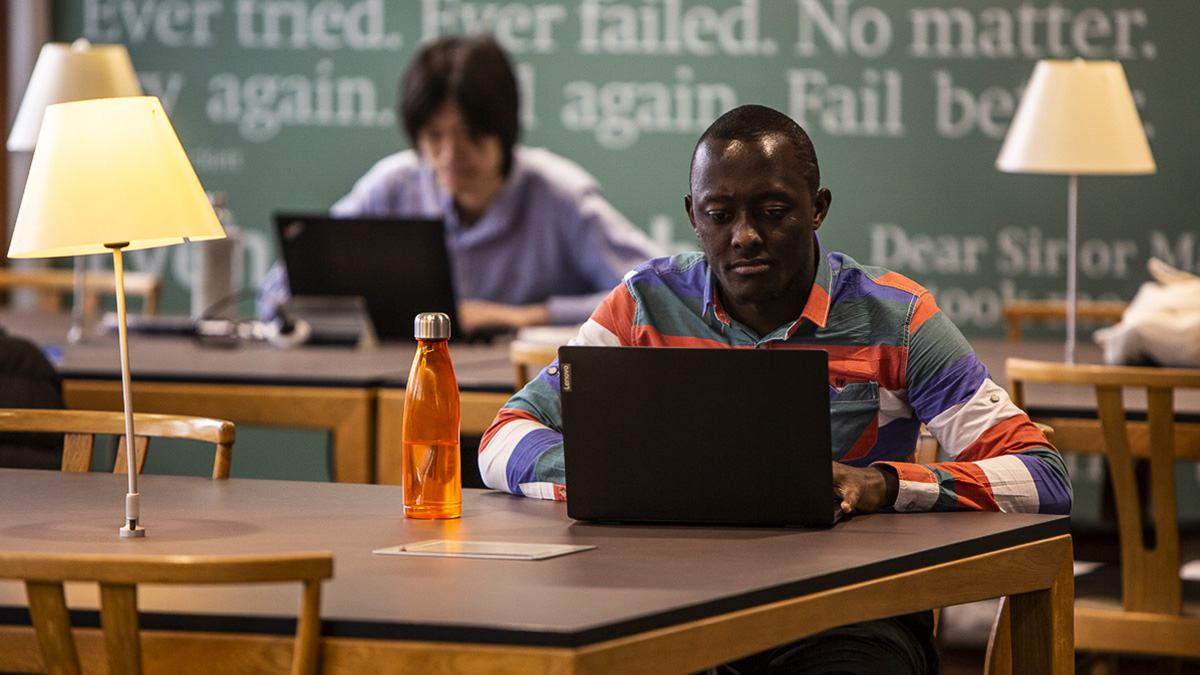 Male student sitting at table in the library studying on laptop