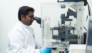 Professor Sakthi Vaiyapuri looking through a microscope in a lab
