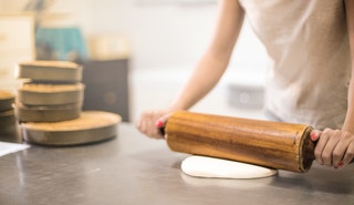 Person in  white t-shirt rolling a pin in dough