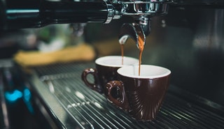 Cafe coffee machine pouring two espressos into brown cups