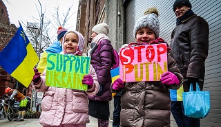 Two girls holding up signs saying Support Ukraine and Stop Putin at a protest against Russian invasion of Ukraine