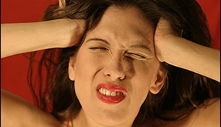 Close up on a woman's face. She is holding her head and grimacing with pain.