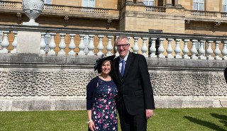 Andrew Charlton-Perez with wife Cristina in smart attire in the Buckingham Palace gardens, with the Palace in the background