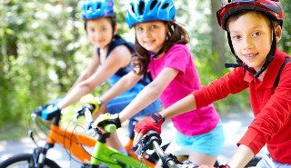 Three children riding bikes and wearing helmets